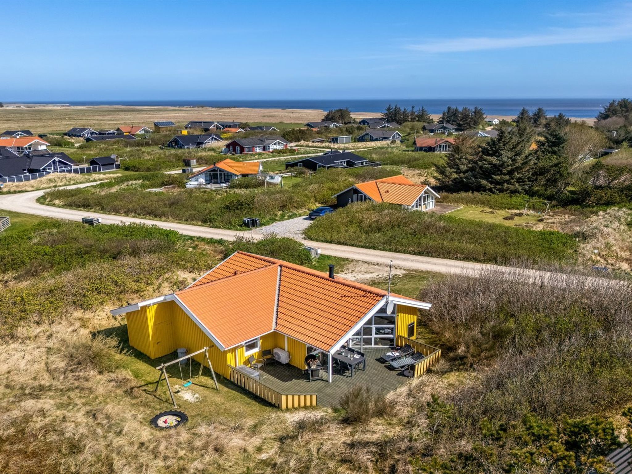 A coastal residential area with houses featuring red roofs and a yellow building with a deck.