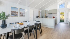 A modern kitchen with white cabinetry, a central island, and a dining area with a white table and black chairs. - "Midja" - 800m from the sea by Interhome (Hvide Sande)