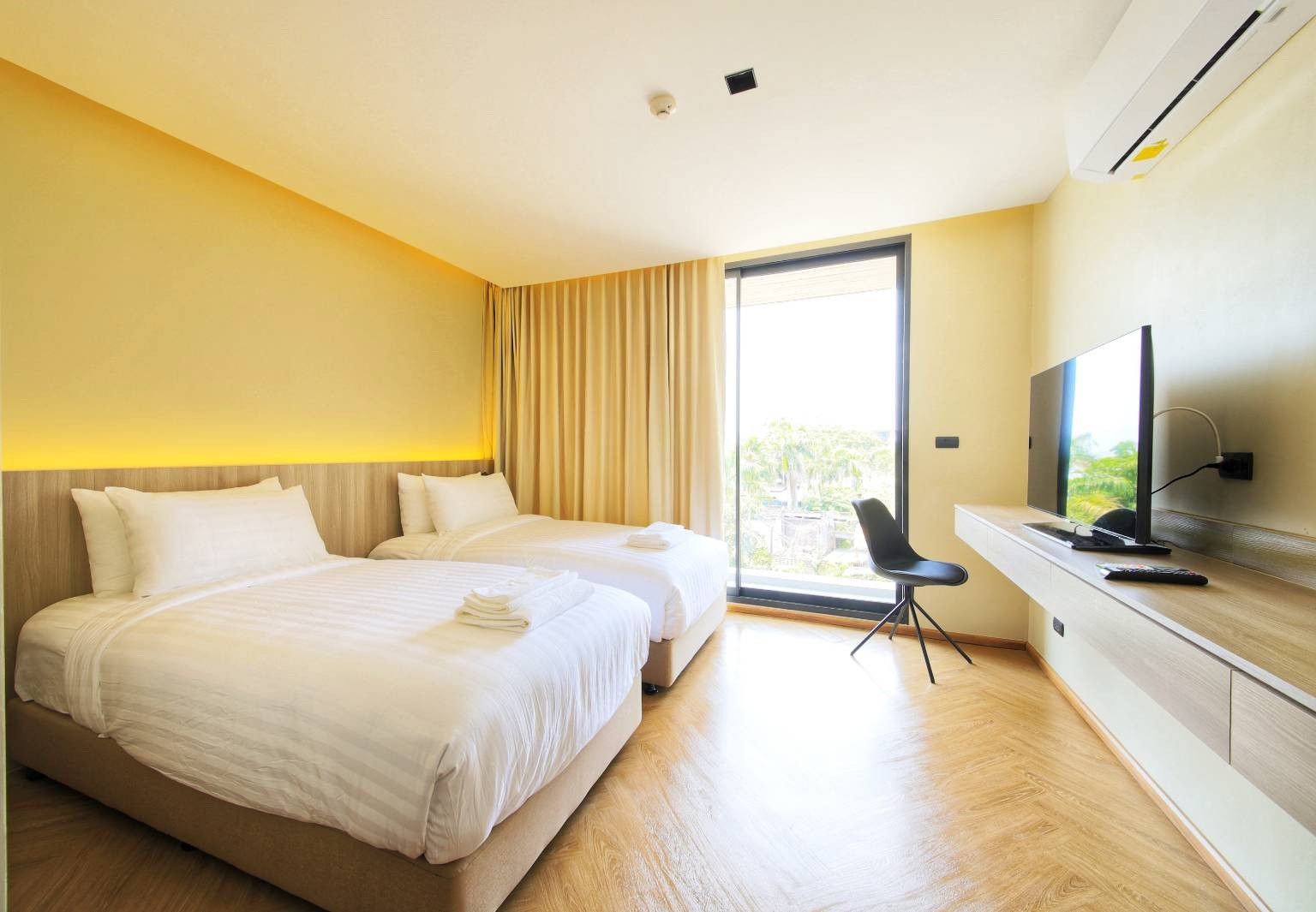 A hotel room with two beds, a TV, and a view of greenery outside.