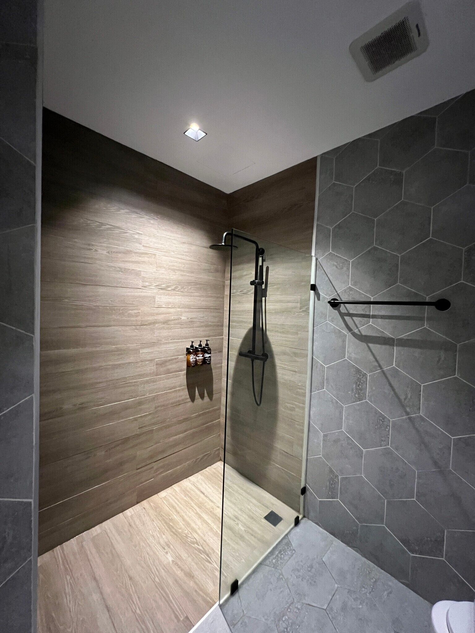 A modern shower with a glass door, wooden wall paneling, and a hexagonal tile pattern on the floor.