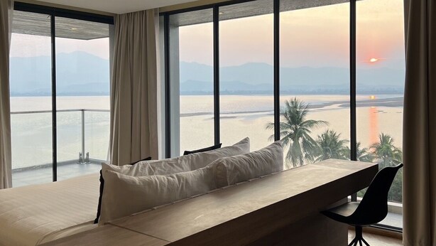 Una habitación de hotel moderna con un amplio ventanal que ofrece vistas al mar y a las montañas.