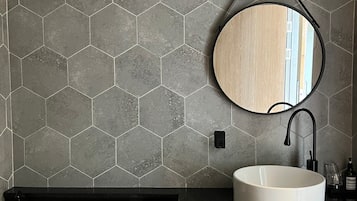 A bathroom with a hexagonal tile backsplash, a round mirror, a white sink, and a toilet.