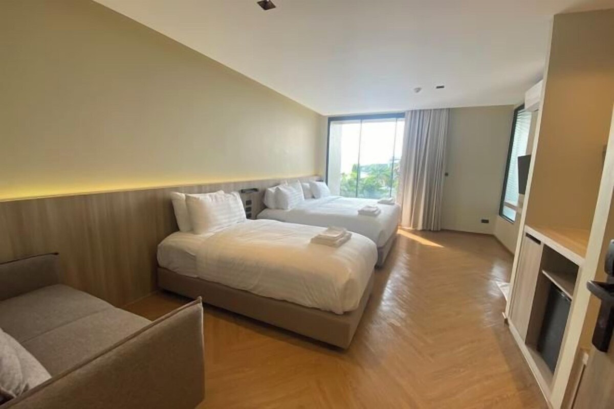 A hotel room with a large bed, a smaller bed, a sofa, and a TV.
