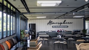 Un interior de restaurante moderno con techos altos, grandes ventanales y un letrero destacado que dice "Atmosphere sky bar & restaurant".