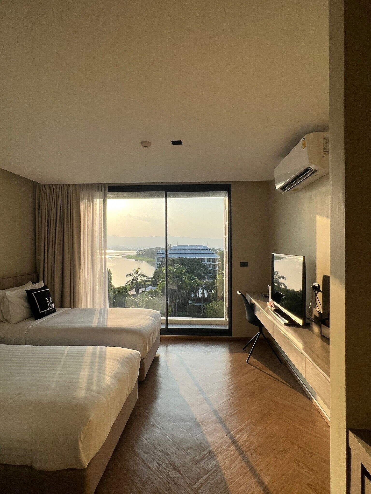 A hotel room with two beds, a TV, and a large window with a city view.