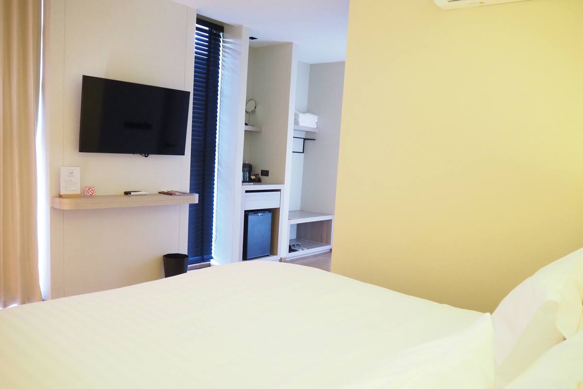 Habitación de hotel con cama, televisor montado en la pared, kitchenette pequeña y baño visible a través de una puerta abierta.