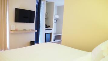 A hotel room with a bed, a television mounted on the wall, a small kitchenette, and a bathroom visible through an open door.
