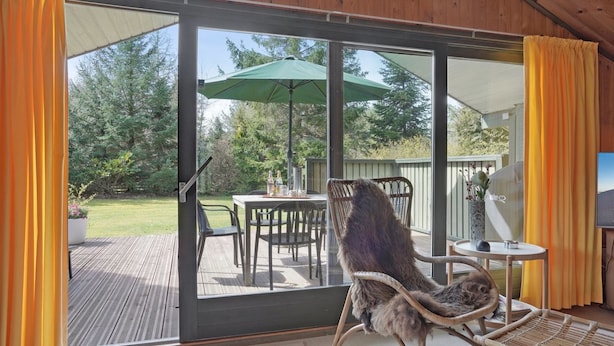 A covered patio area with a table, chairs, and a wicker chair with a cushion.