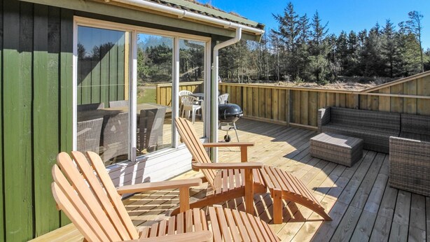 Eine Holzterrasse mit Gartenmöbeln, einem Grill und einer Glastür zu einem überdachten Bereich.