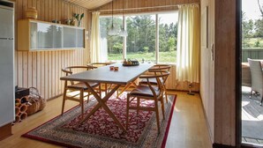 Ein Holzinterieur mit Esstisch, Stühlen, einem Teppich und Blick ins Freie.