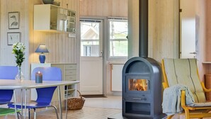 Ein gemütlicher Raum mit Kaminofen, einem Esstisch mit Stühlen, einer Lampe und einem Sessel mit Decke.