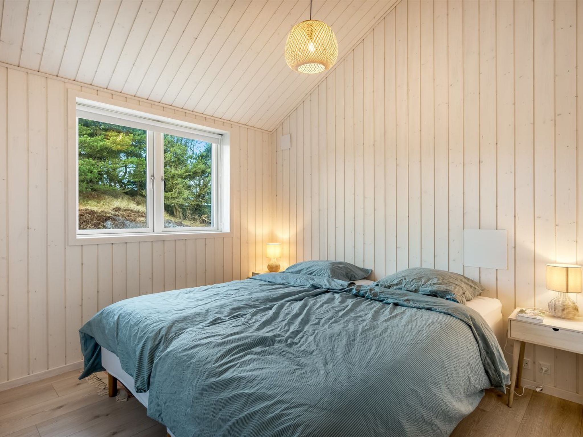 Une chambre à coucher avec un lit, une fenêtre, une table de chevet et un luminaire suspendu.