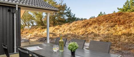 Un patio al aire libre con una mesa, sillas, una pérgola y vistas a una colina.
