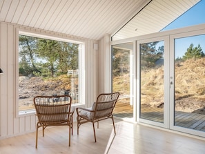 Ein Zimmer mit zwei Korbstühlen, großen Fenstern und Blick auf eine natürliche Landschaft.
