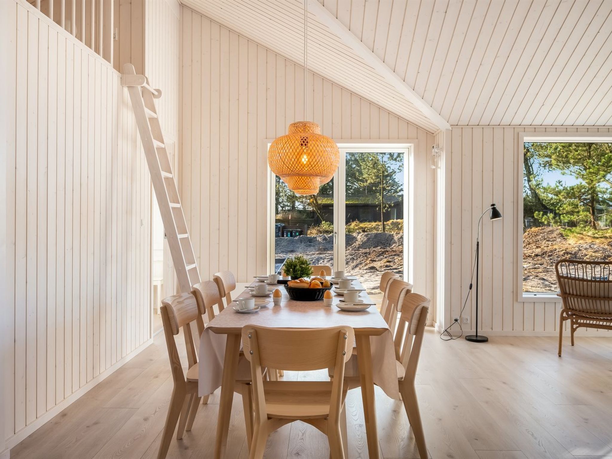 A dining area with a wooden table and chairs, a hanging light fixture, and a view of the outdoors.