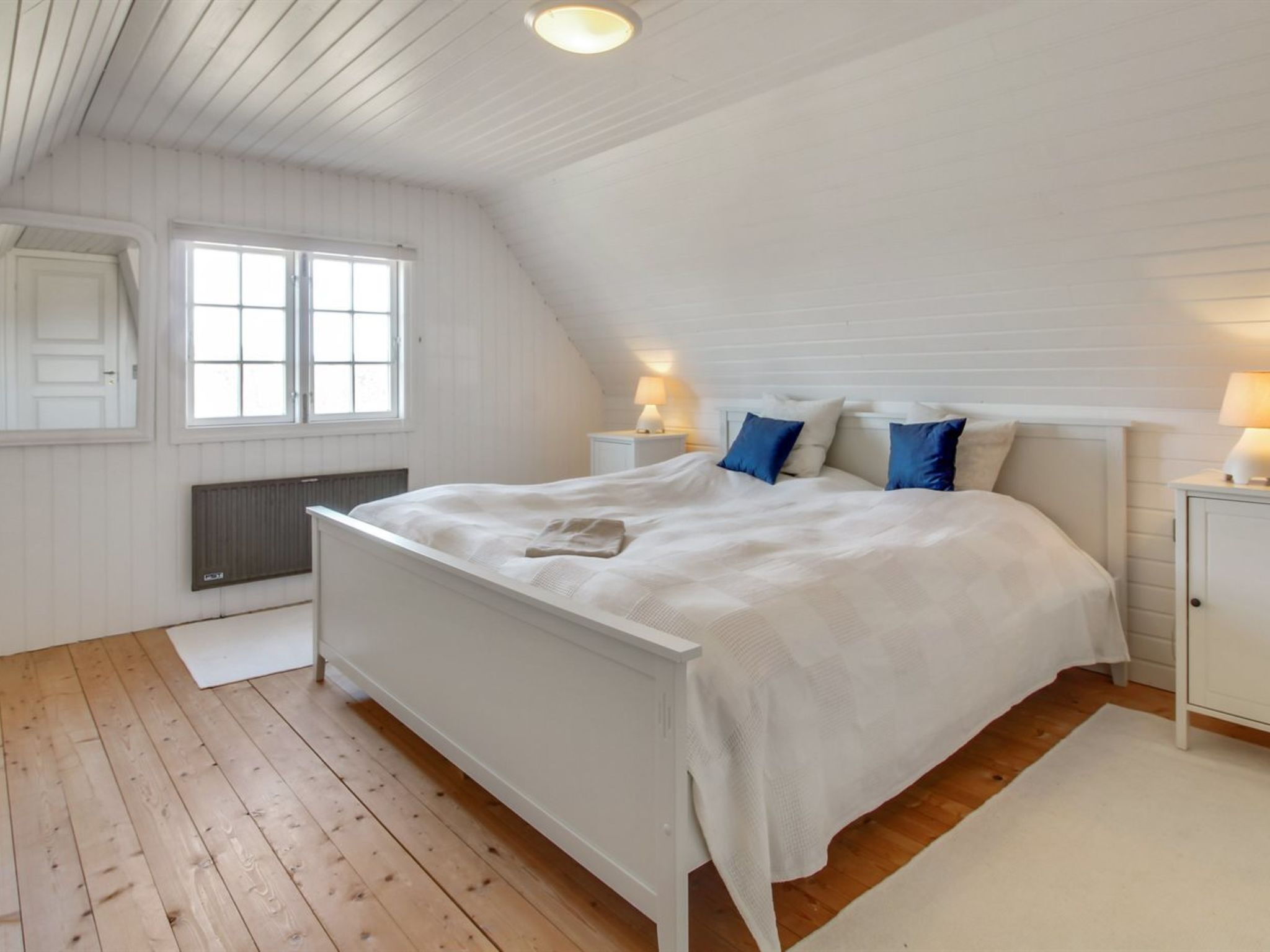 Een slaapkamer met een wit bed, twee nachtkastjes, een raam en een radiator.