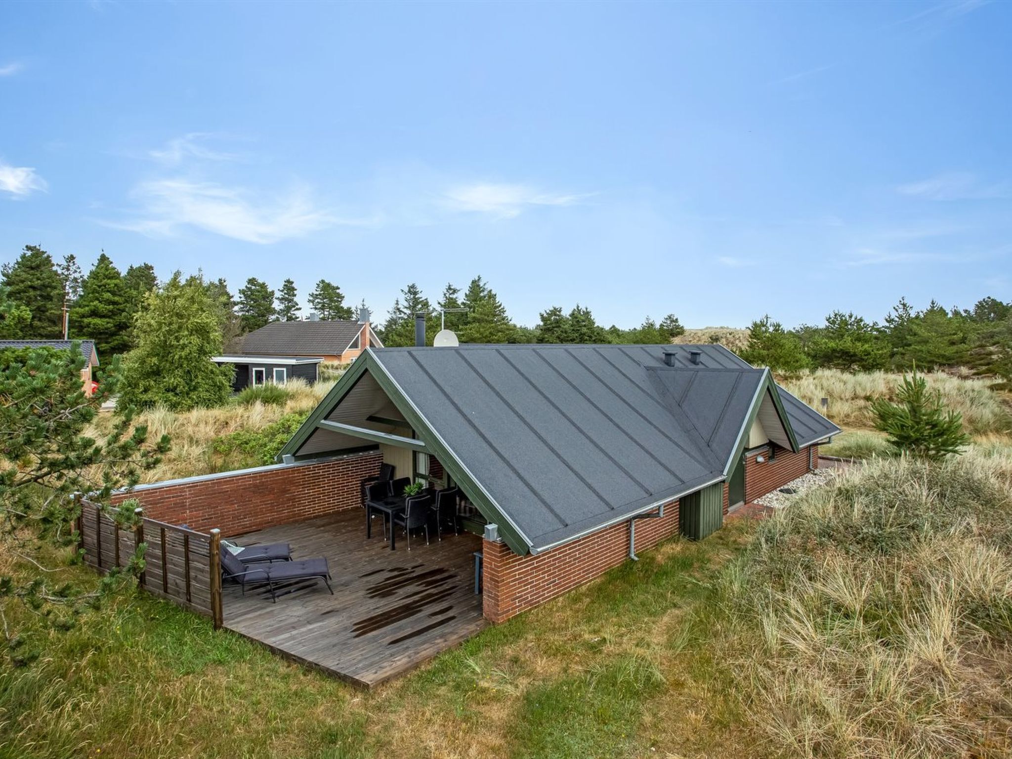 A modern house with a sloped roof, a patio with outdoor furniture, and a brick exterior.