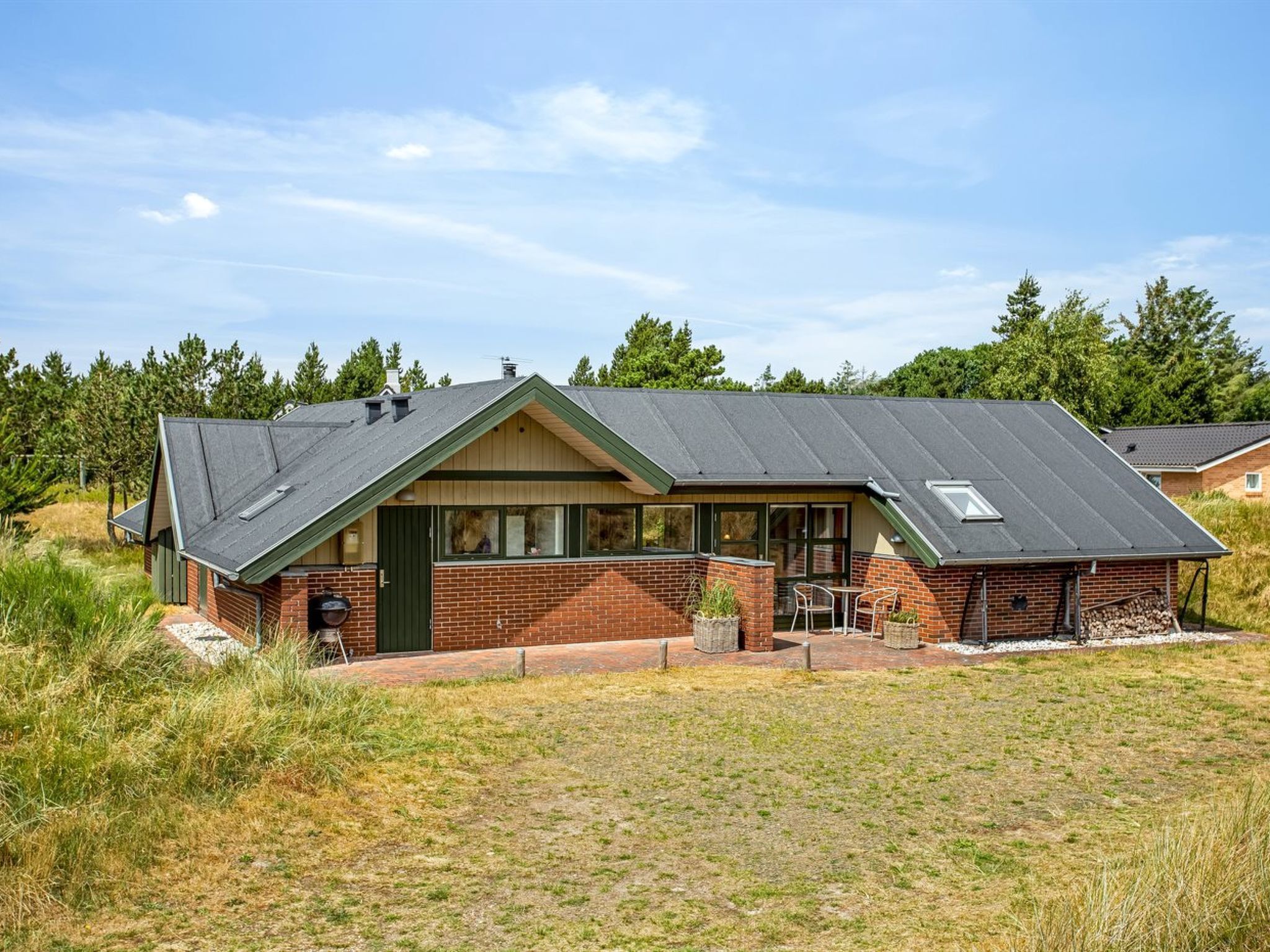 A single-story house with a sloped roof, brick exterior, and a small porch with outdoor seating.