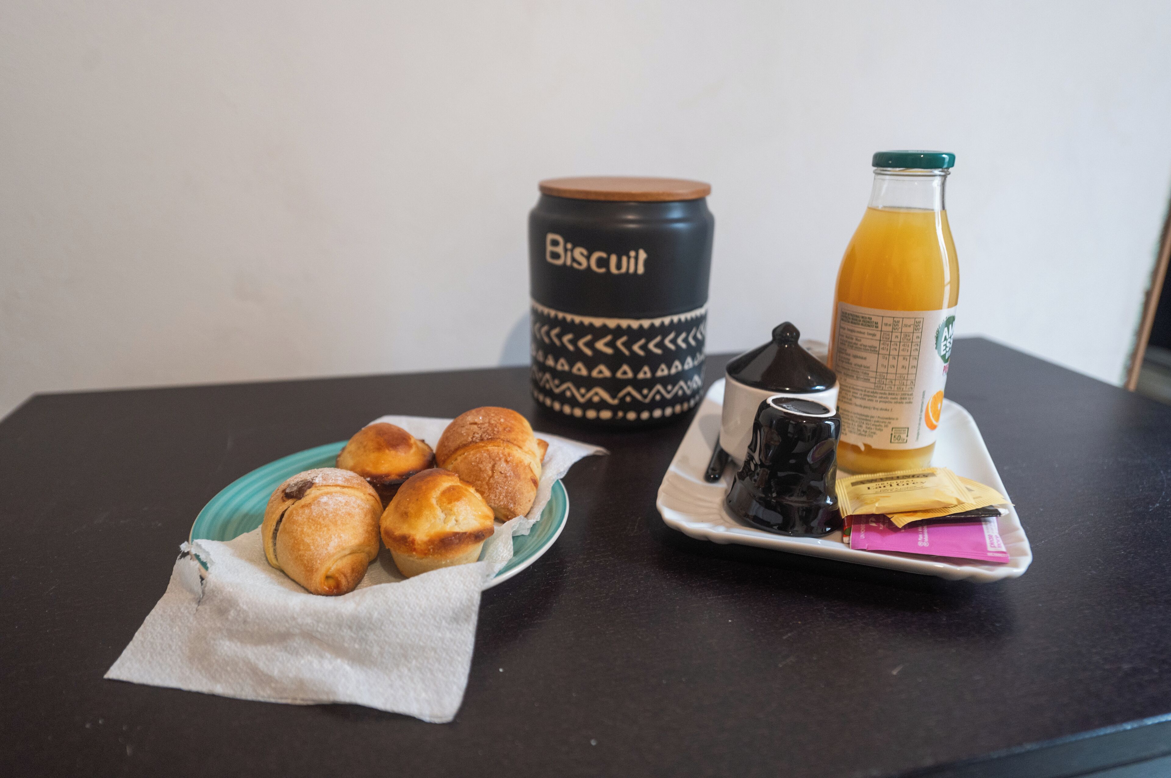 Un vassoio per la colazione con dolci, una scatola per i biscotti, una bottiglia di succo d'arancia e un teiera.