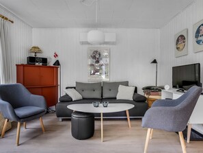 Un salon moderne avec un canapé gris, deux fauteuils, une table basse, un téléviseur et une bibliothèque.