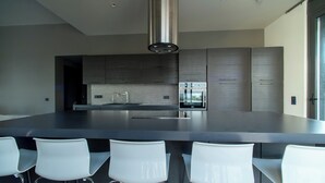 A modern kitchen with a central island, stainless steel appliances, and white bar stools. - Minimal brand new villa with private pool close to Athens (Kalamos)