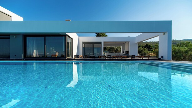 A modern poolside area with a clear blue pool, large sliding glass doors, and outdoor seating. - Minimal brand new villa with private pool close to Athens (Kalamos)