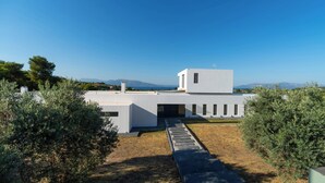 A modern building with a flat roof, a central entrance, and a view of the sea in the background. - Minimal brand new villa with private pool close to Athens (Kalamos)