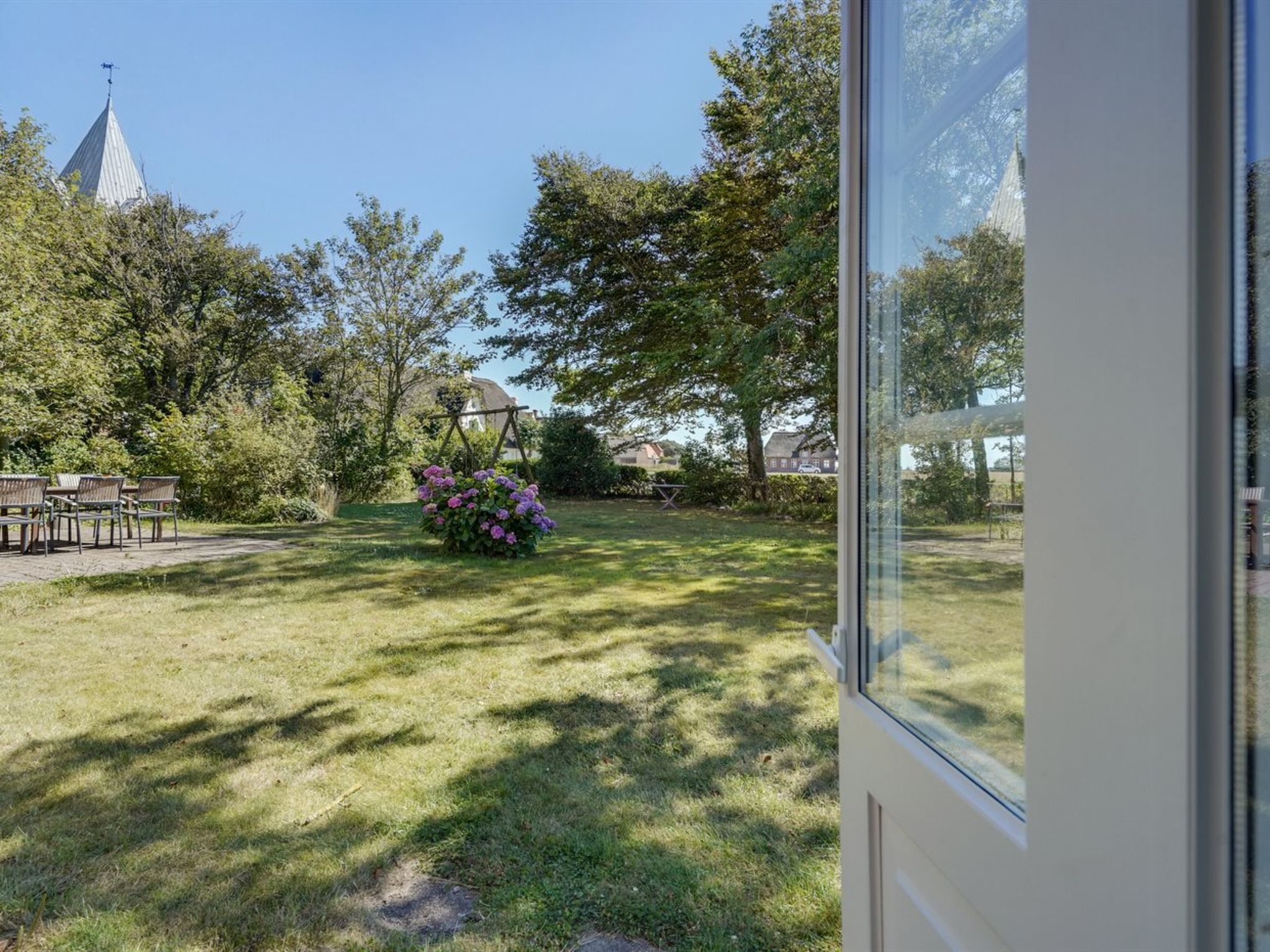 Un jardin agrémenté d’un belvédère, d’une pelouse et d’un bâtiment avec une tour en arrière-plan.