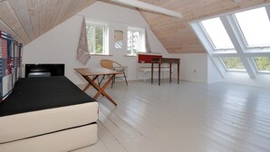 A spacious attic bedroom with a sloped ceiling, a bed, a desk, a chair, and large windows.