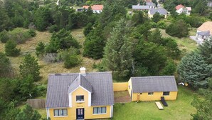 A yellow two-story house with a grey roof, surrounded by greenery and other houses in a rural setting.