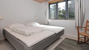 A bedroom with a bed, two bedside lamps, a window with curtains, a wooden ceiling, and a view of trees outside.