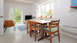 A dining area with a wooden table and chairs, a television, and a window with curtains.