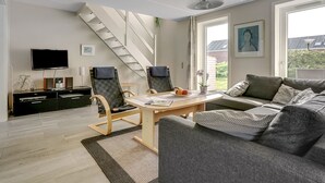 A modern living room with a staircase, a flat-screen TV, a dining table, and a sofa.