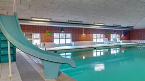 An indoor swimming pool with a slide, a brick wall, and a seating area with chairs and a table.