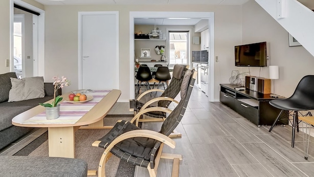 A modern apartment with a dining area, a living room, and a kitchen. There is a staircase leading to an upper level.