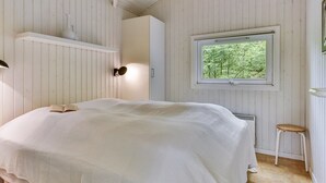 Une chambre à coucher avec un lit, une fenêtre donnant sur des arbres, une armoire blanche et un petit tabouret.