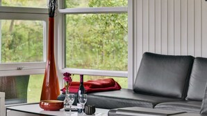 Un salon moderne avec un canapé en cuir, une table basse en verre et une vue sur la verdure grâce à de grandes fenêtres.