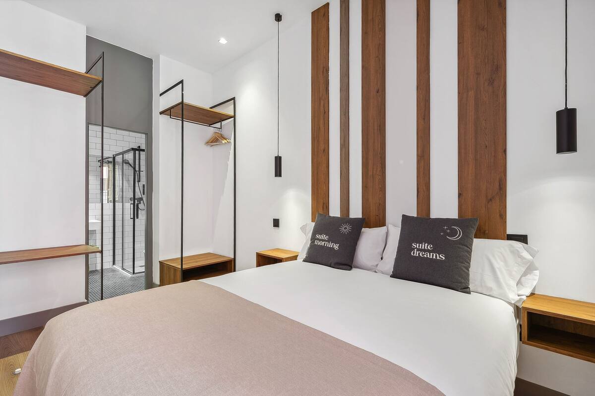 Ein modernes Hotelzimmer mit einem großen Bett, einem Holzkopfende und einer Duschkabine aus Glas.