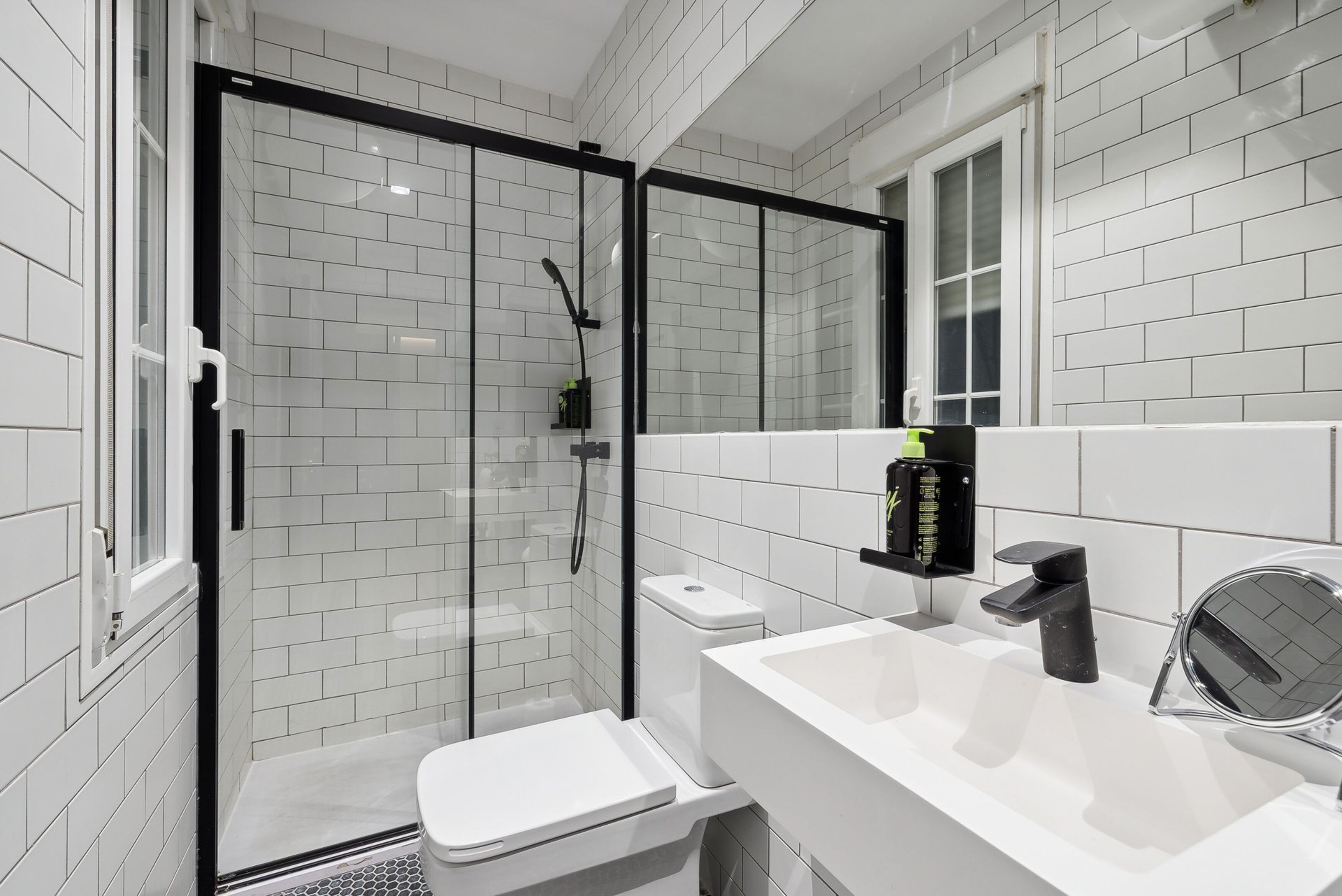 A modern bathroom with a glass-enclosed shower, a white toilet, a sink with a black faucet, and a mirror.