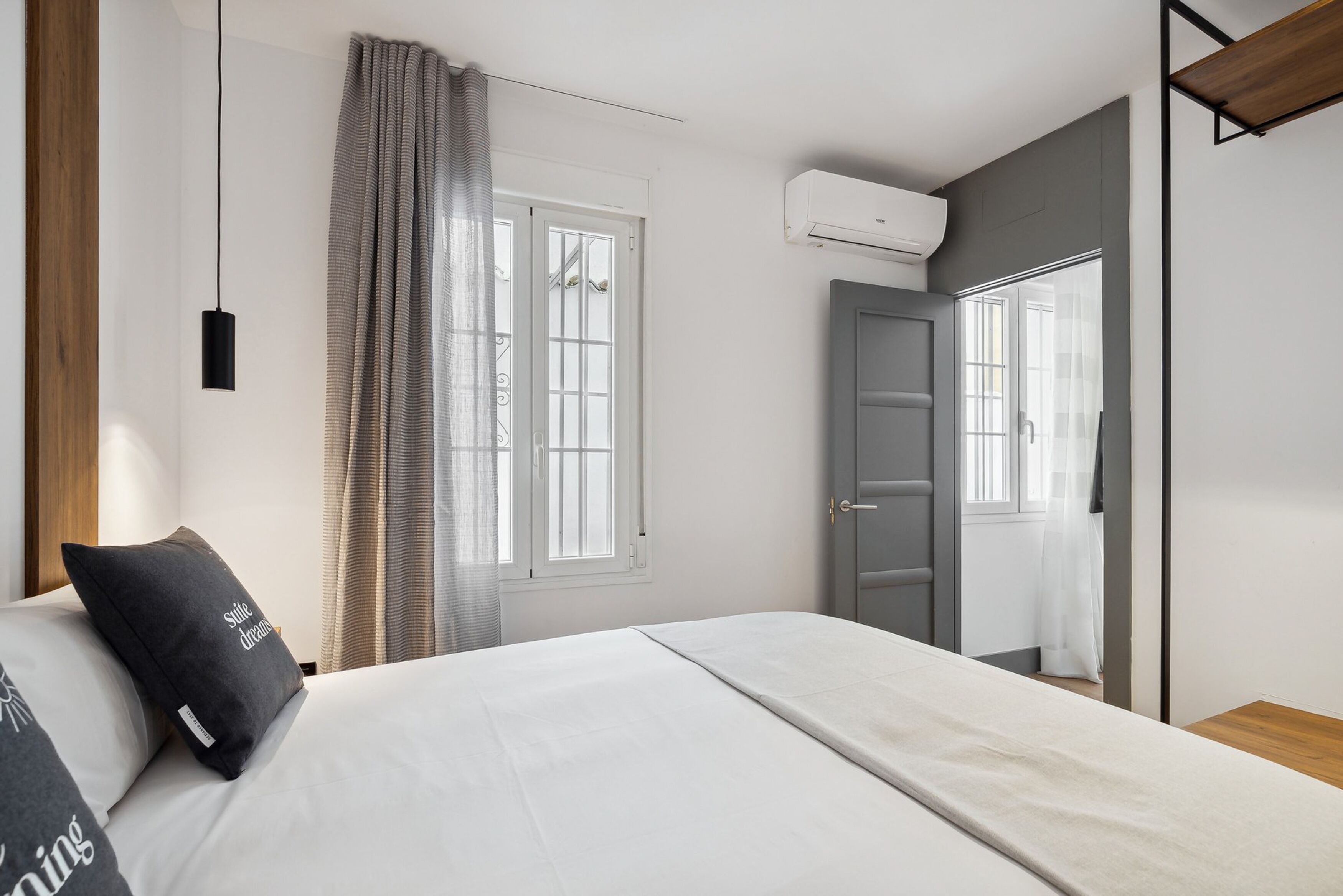 Un dormitorio con cama, ventana con cortinas, equipo de aire acondicionado y puerta.