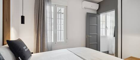 Un dormitorio con cama, ventana con cortinas, equipo de aire acondicionado y puerta.