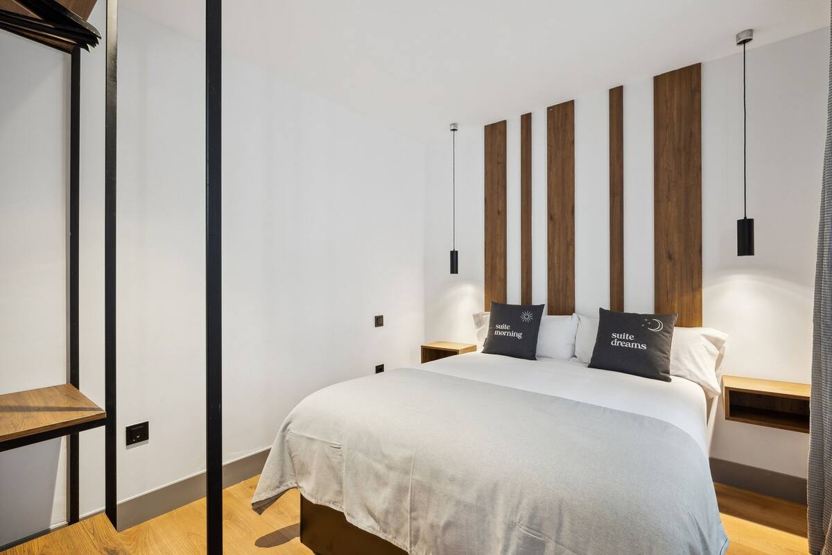 Ein modernes Schlafzimmer mit einem großen Bett, einem Holzkopfende, Nachttischen und einer hängenden Pendelleuchte.