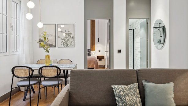 Ein modernes Wohnzimmer mit einer Couch, einem Esstisch und Stühlen. Ein Flur führt zu einem Badezimmer mit einer Glasdusche.