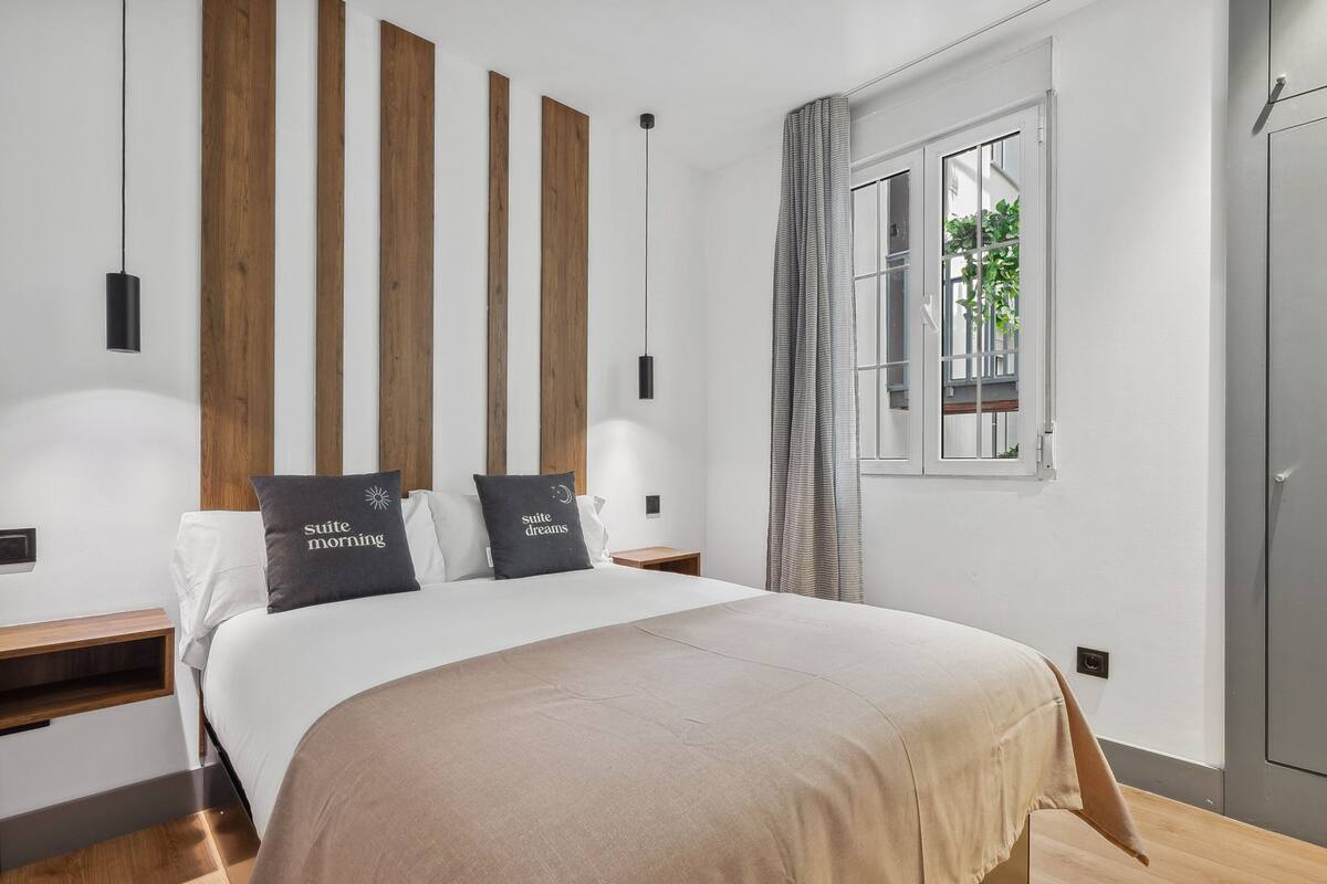 Ein modernes Schlafzimmer mit einem großen Bett, einem Holzkopfende, Nachttischen und einem Fenster mit Vorhängen.