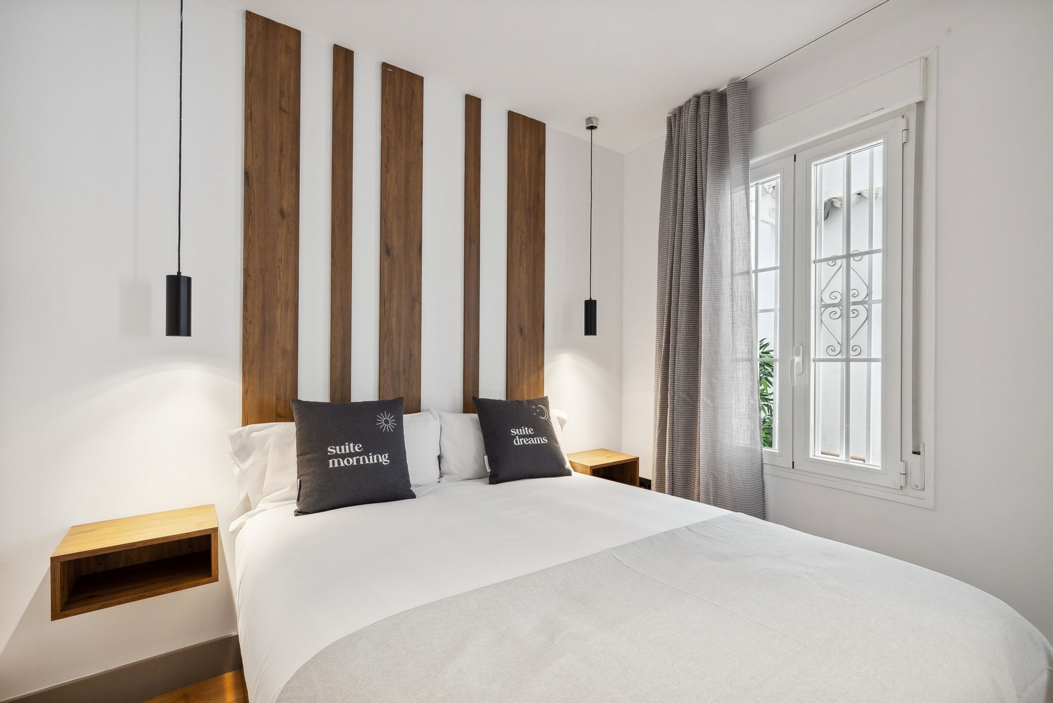 A modern bedroom with a large bed, wooden headboard, two bedside tables, and a window with curtains.