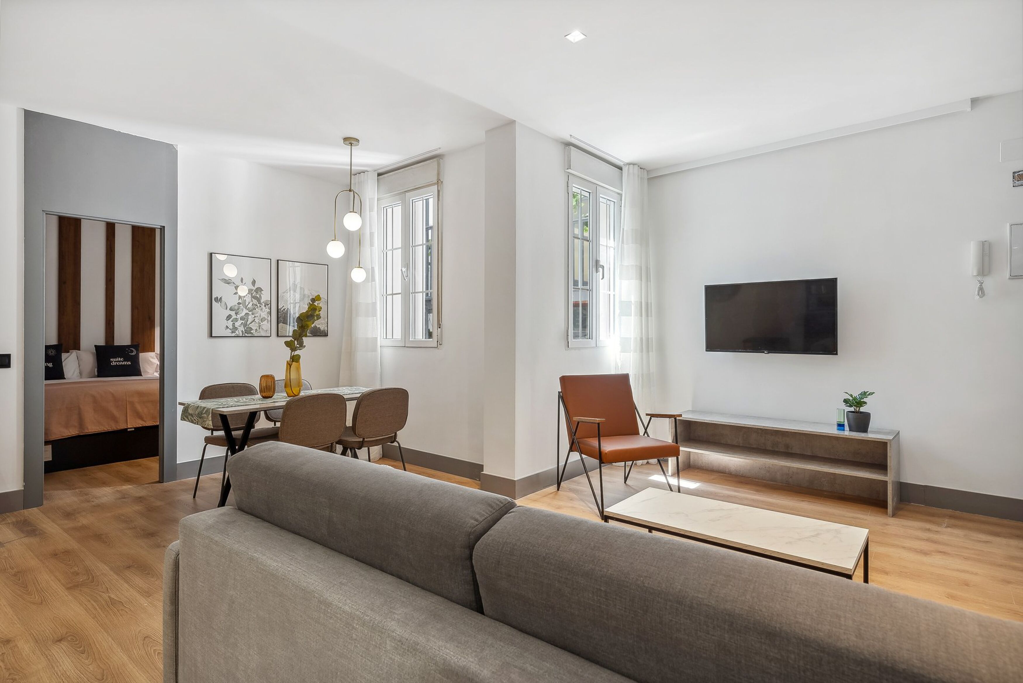 A modern living room with a sofa, dining table, chairs, and a TV.