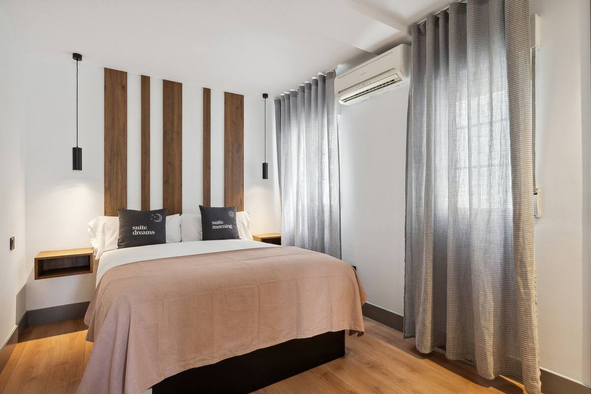Ein modernes Schlafzimmer mit Bett, Holz-Kopfteil, Nachttischen und einem Fenster mit Vorhängen.