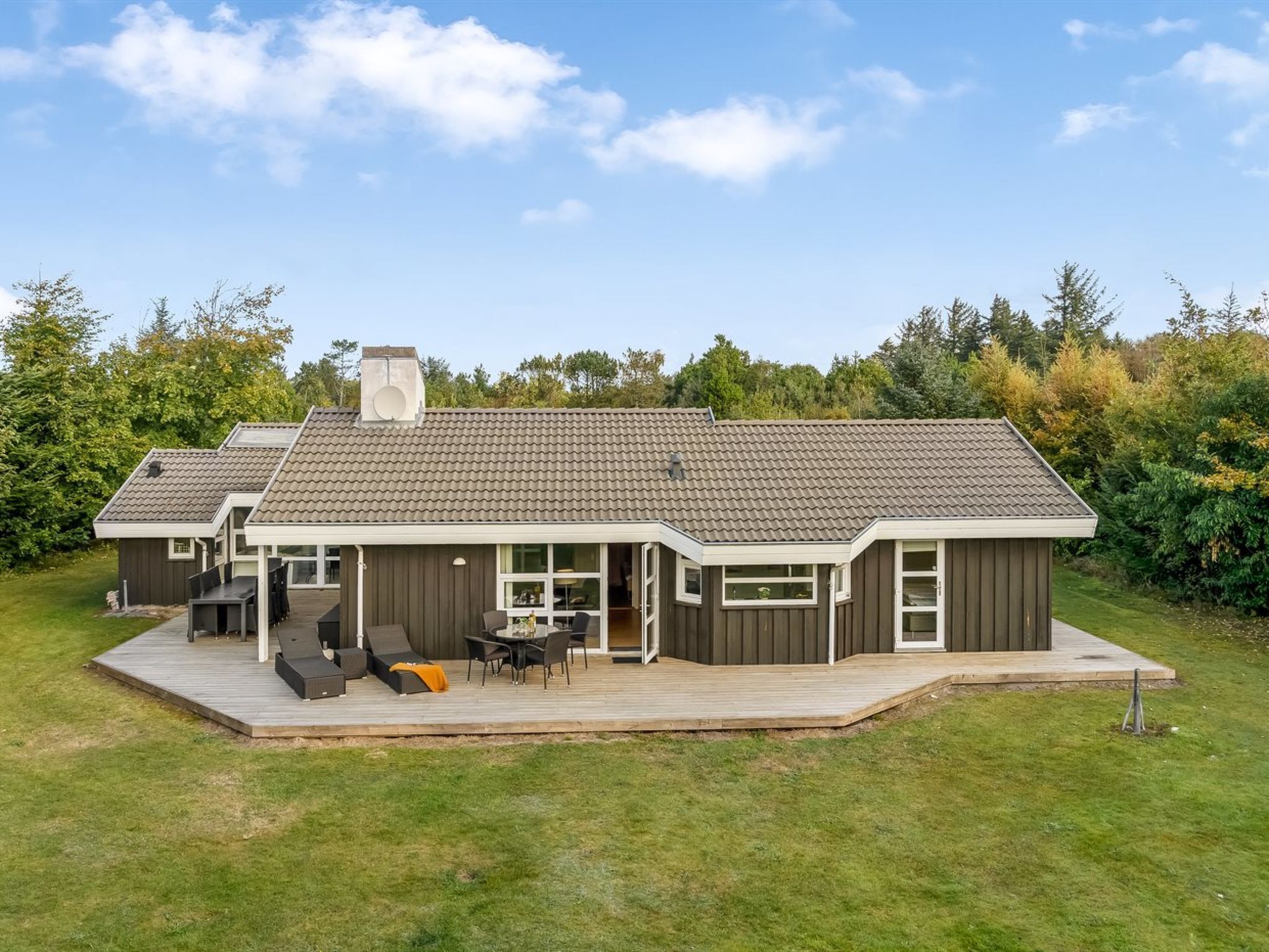Ein modernes, zweistöckiges Haus mit überdachter Terrasse und einer Holzterrasse.