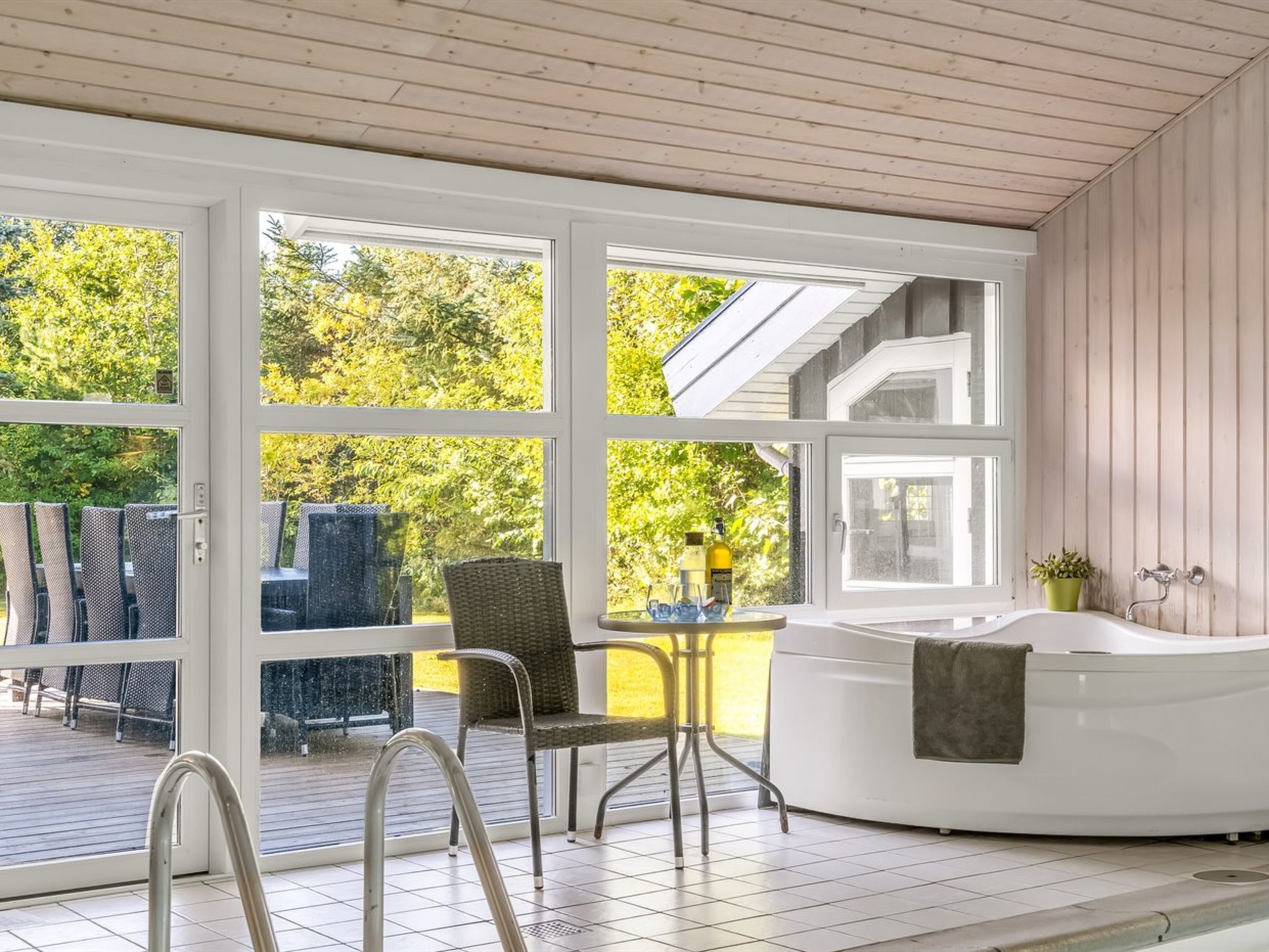 A sunlit room with a hot tub, large windows, and a view of greenery outside.