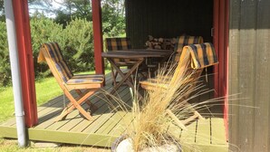 En træterrasse med et bord og stole, en potteplante og en stabel brænde.